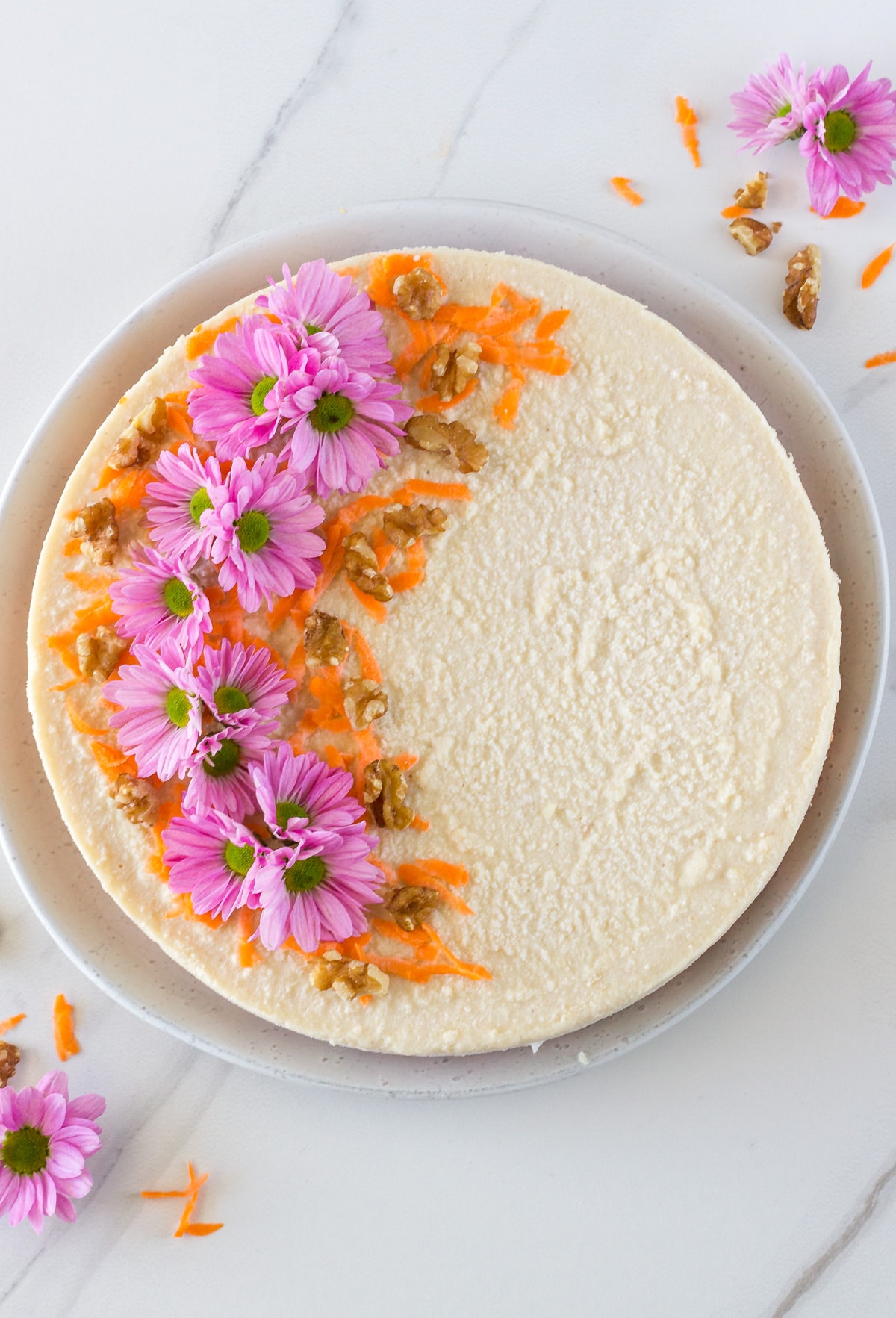 No-bake carrot cake decorated with flowers, shredded carrot and walnuts. 