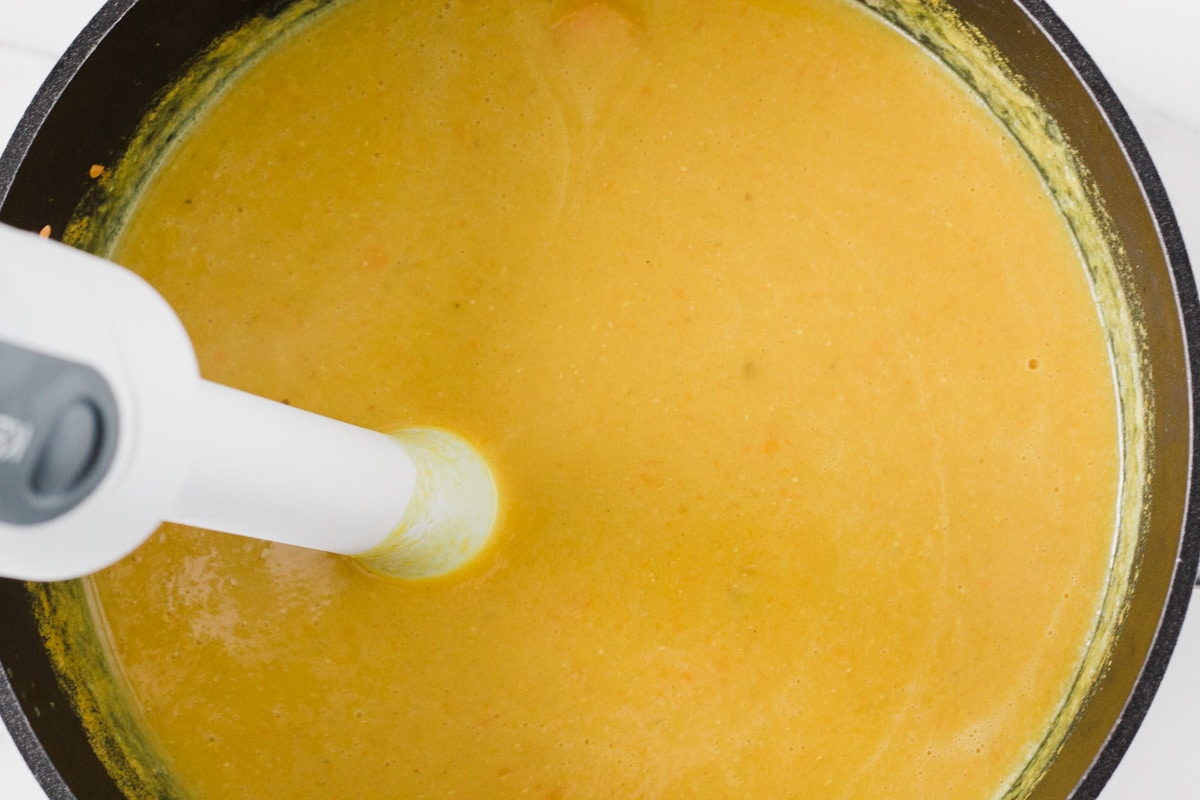 The soup being blended with a hand stick blender.