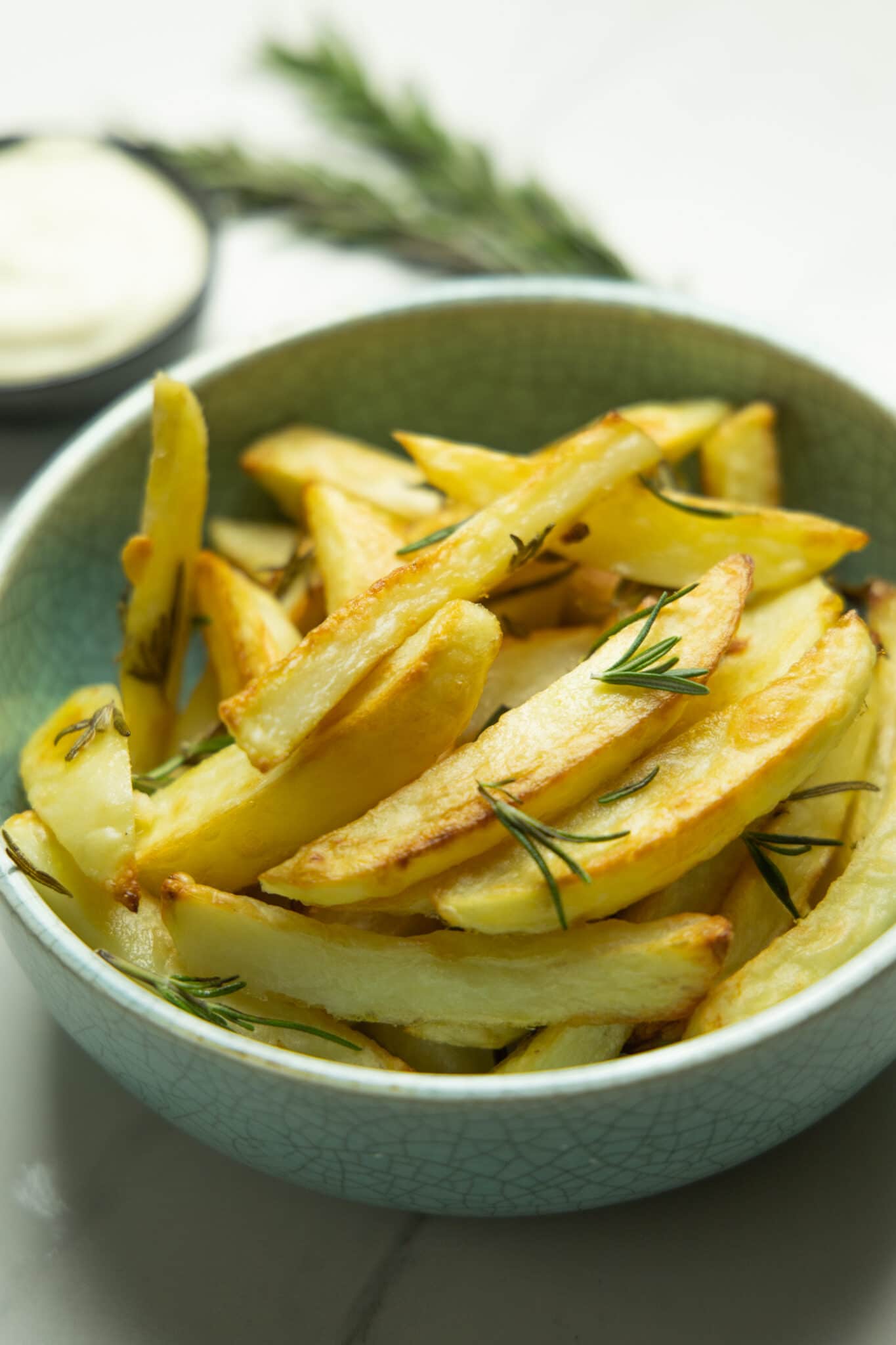 photo of the fries in a bowl with aioli and rosemary in the background