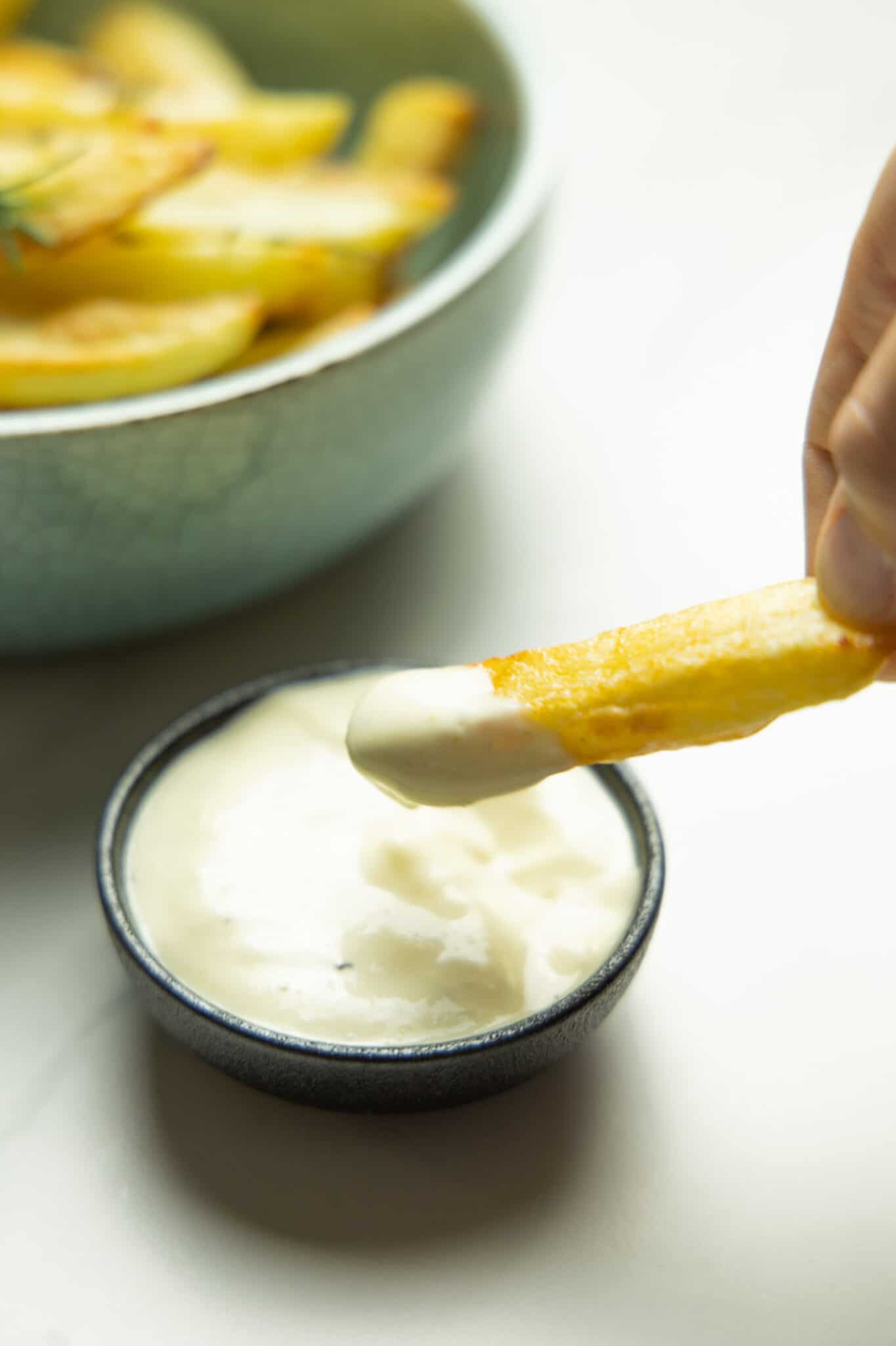 photo of one of the fries being dipped in aioli in front of a bowl of oven baked fries