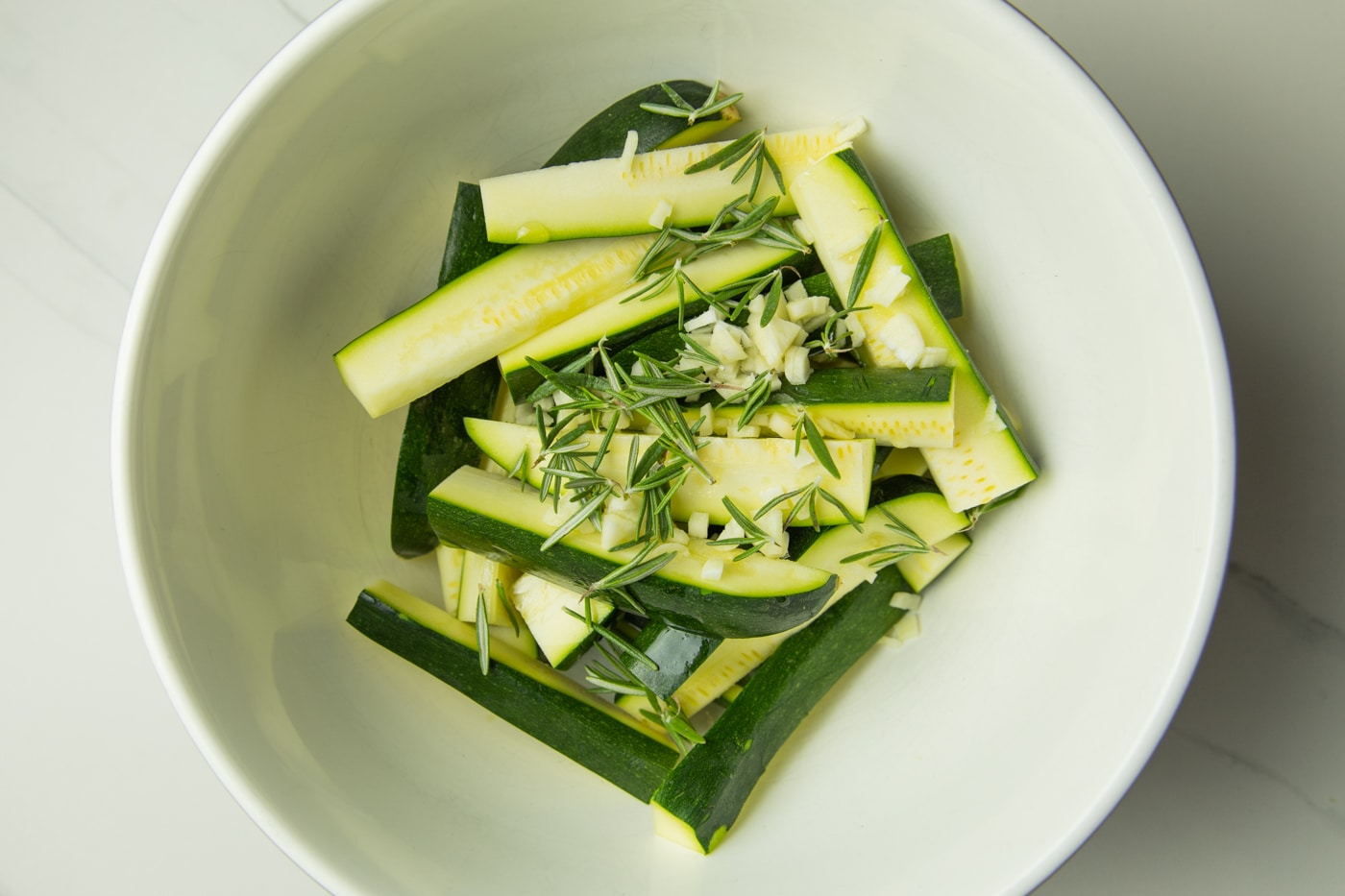 bowl of zucchini wedges with rosemary, garlic and spices