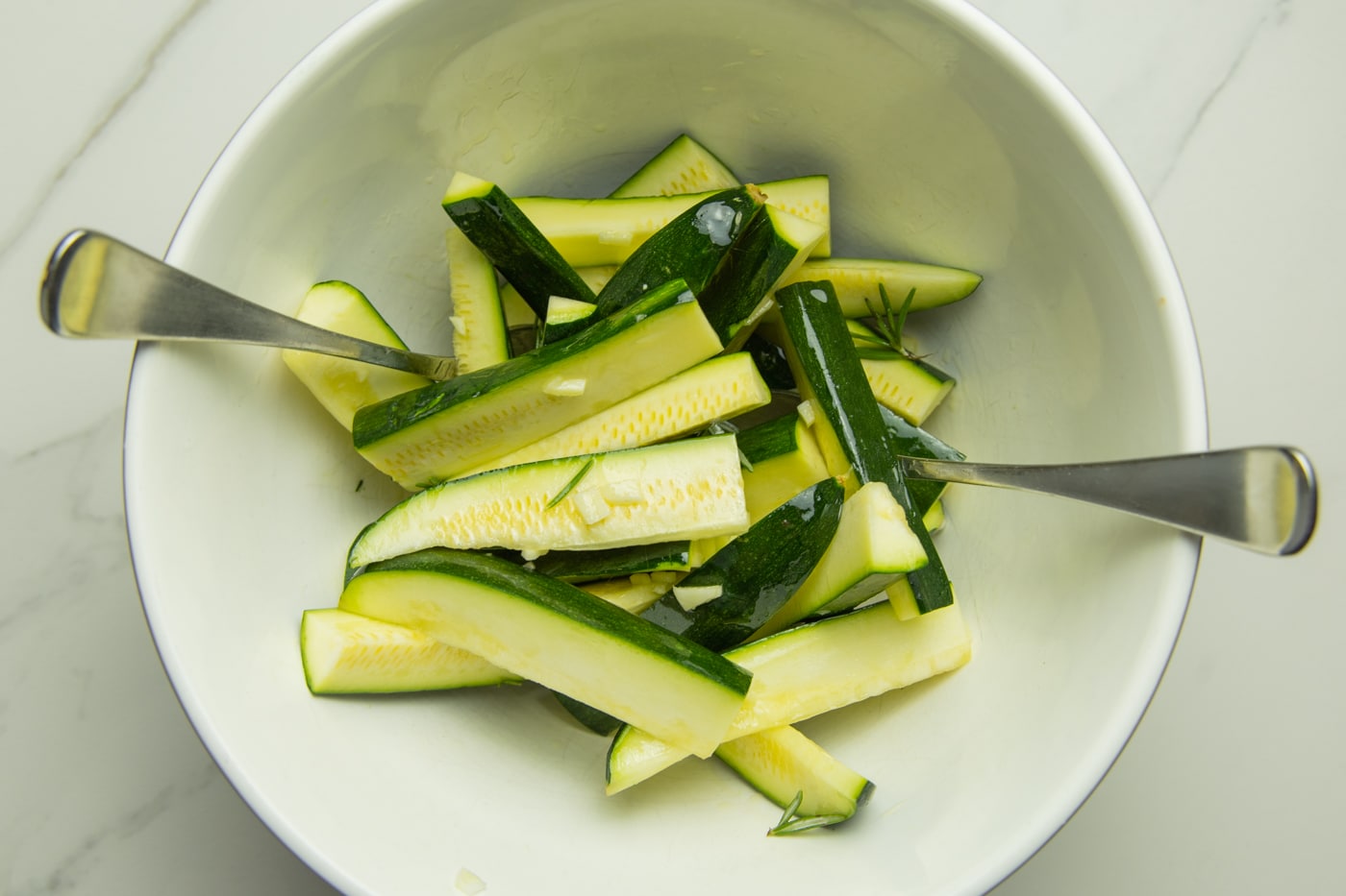 bowl of zucchini wedges with rosemary, garlic and spices mixed together