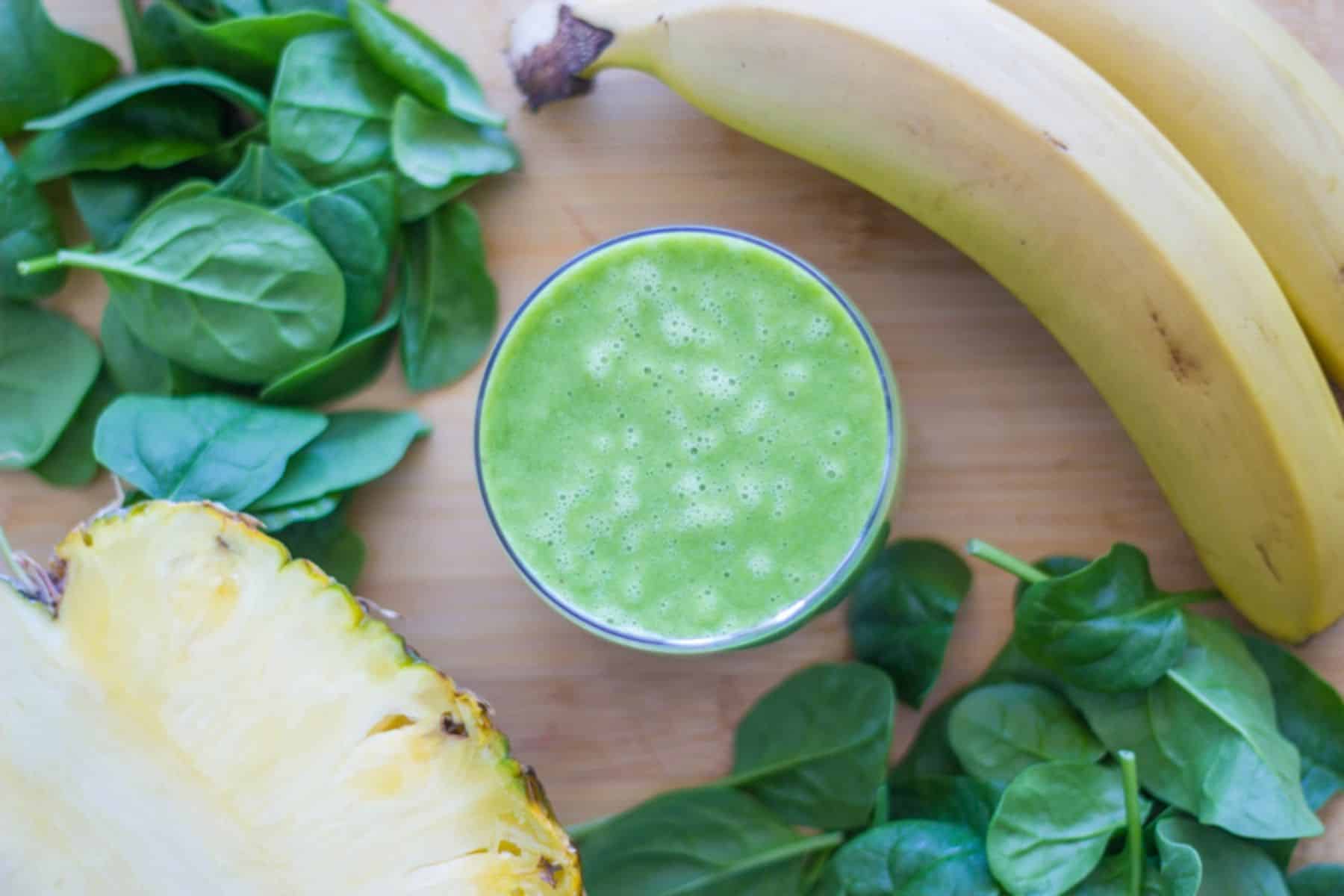 A glass of the green smoothie with the ingredients used to make it around the glass.