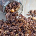A jar of chocolate granola spilled on a wooden board.