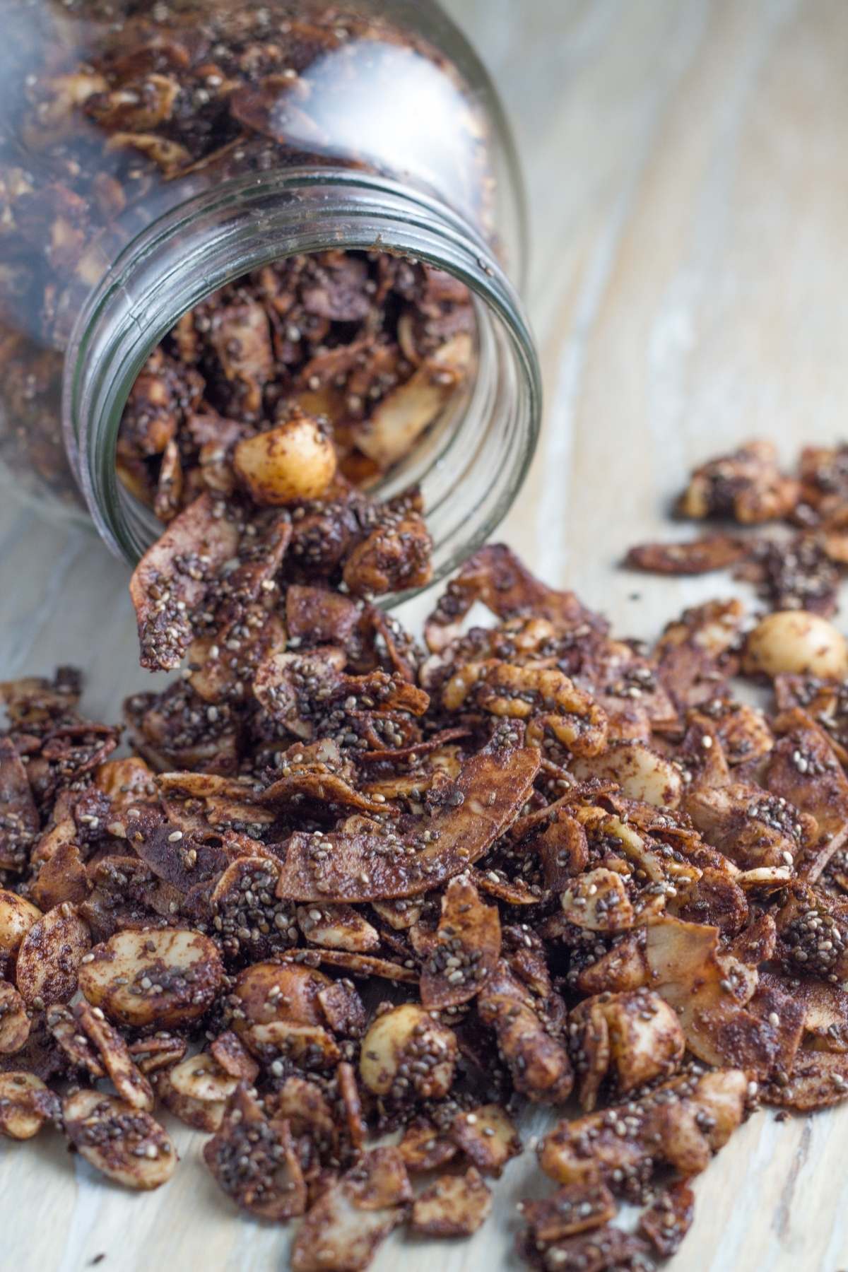 A jar of gluten free chocolate granola spilled on a wooden board.