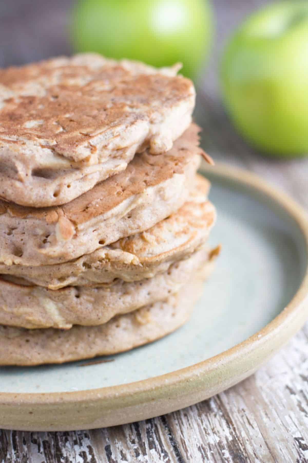 Stack of apple cinnamon pancakes on a plate with some apple behind it.