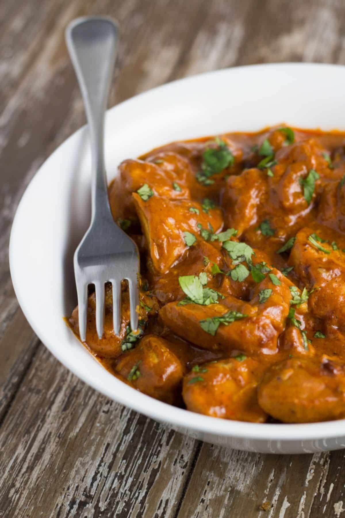 A bowl of slow cooker butter chicken with some fresh coriander on top. 