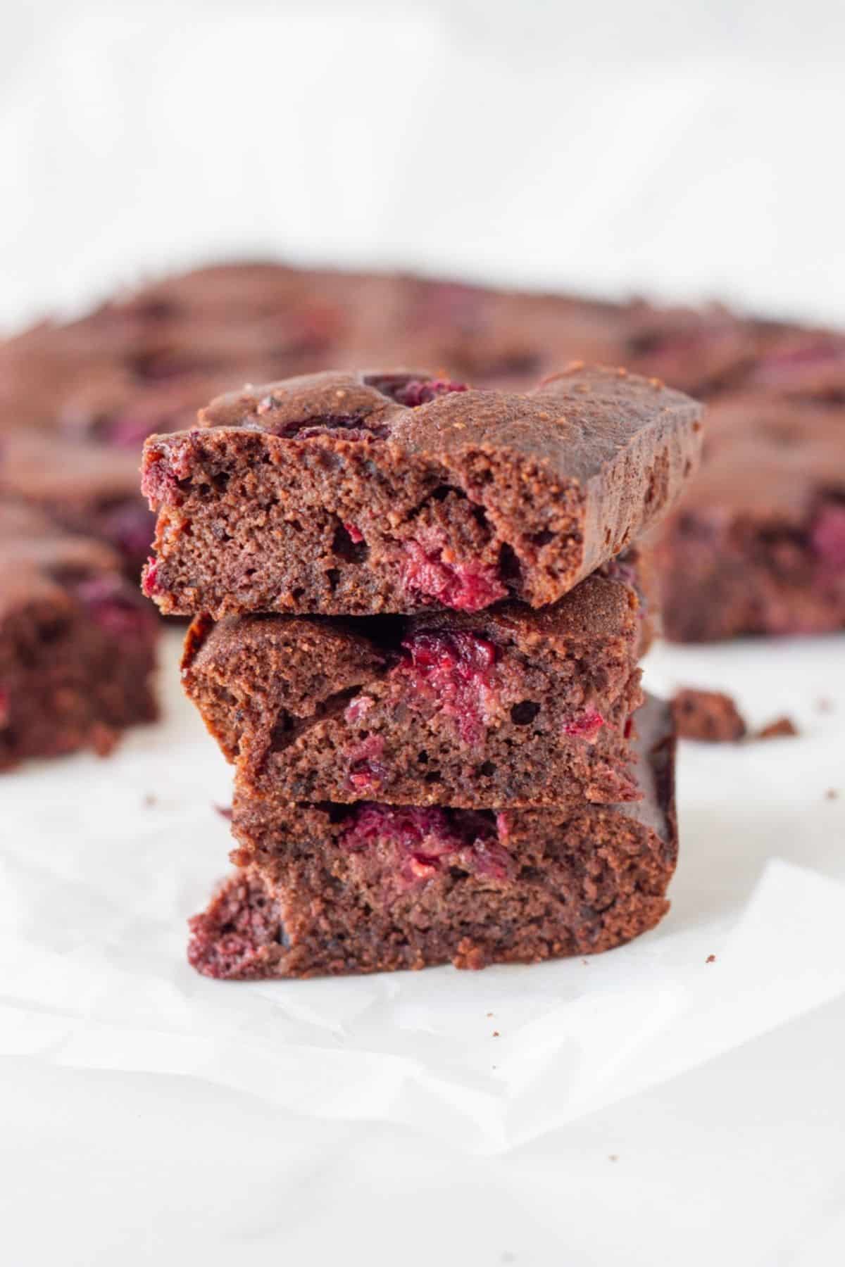 Three raspberry brownies stacked on top of each other with the remaining brownies behind them.