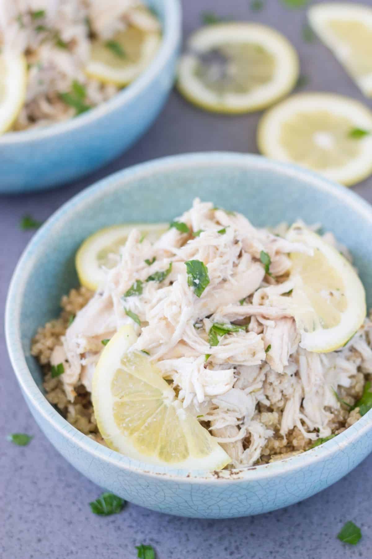 A bowl slow cooked pulled chicken topped with fresh lemon and herbs.