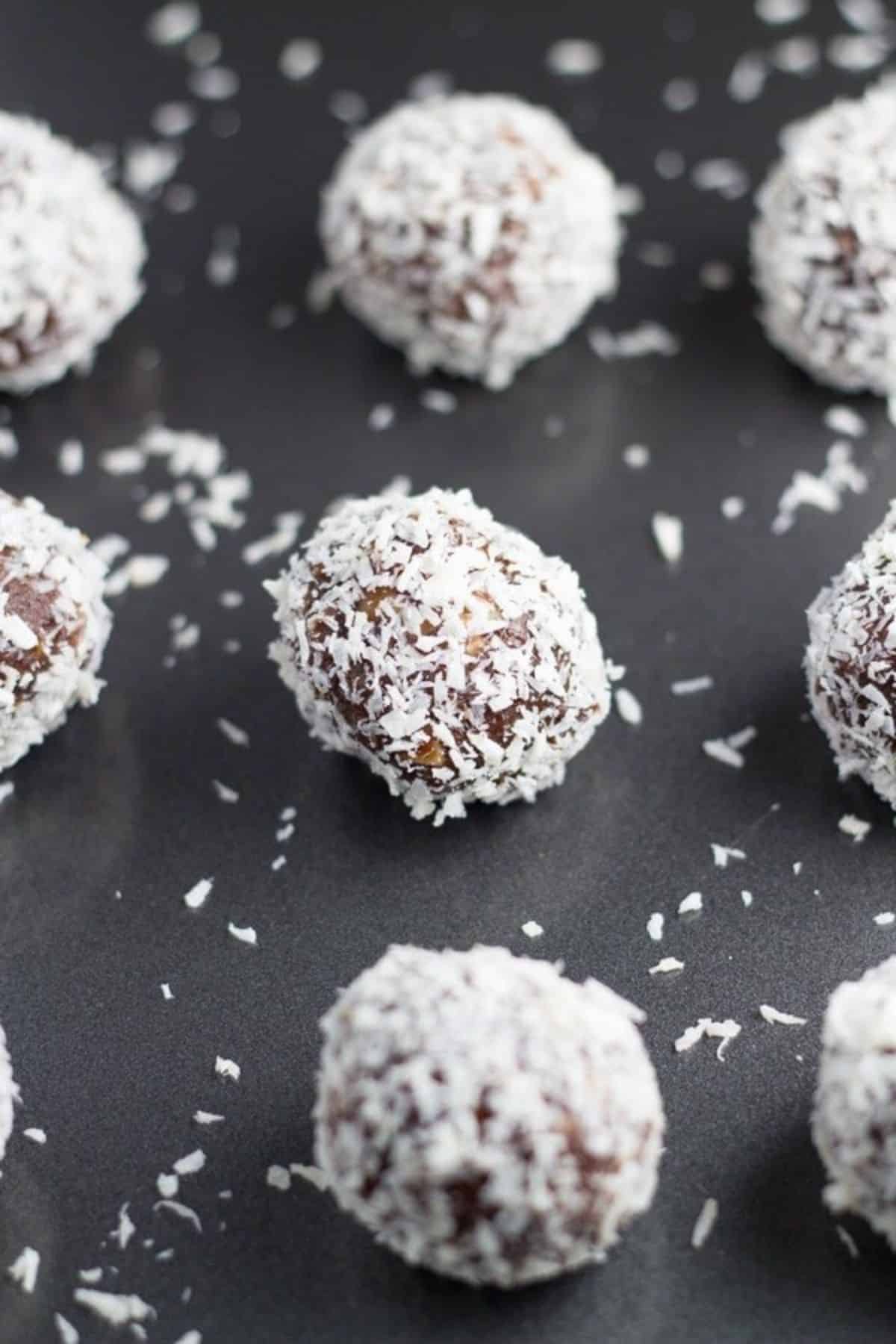 Chocolate peppermint balls on a black tray with shredded coconut around them.