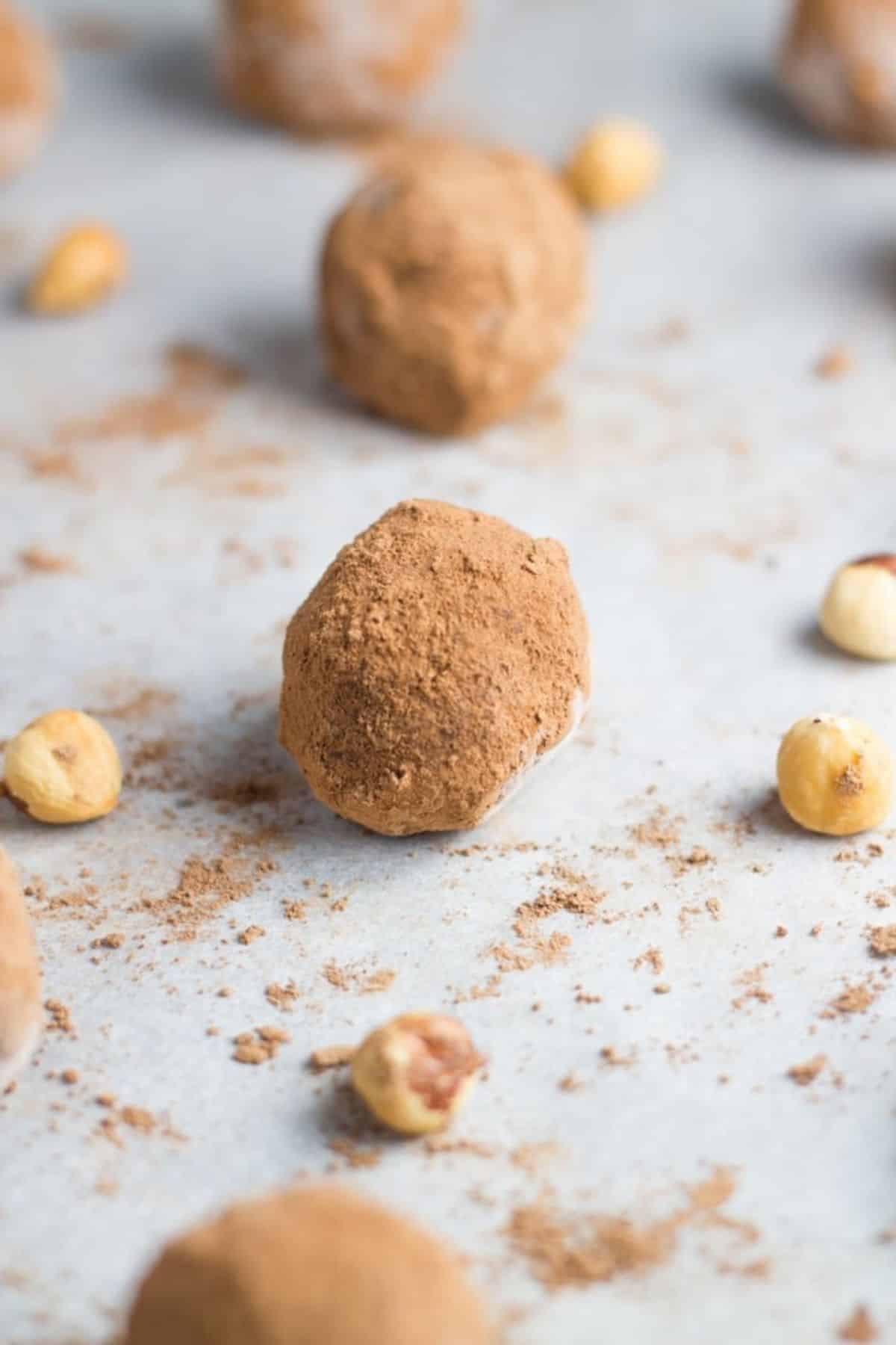 Nutella Truffles on a baking tray lined with baking paper with hazelnuts and cacao powder sprinkled around them.